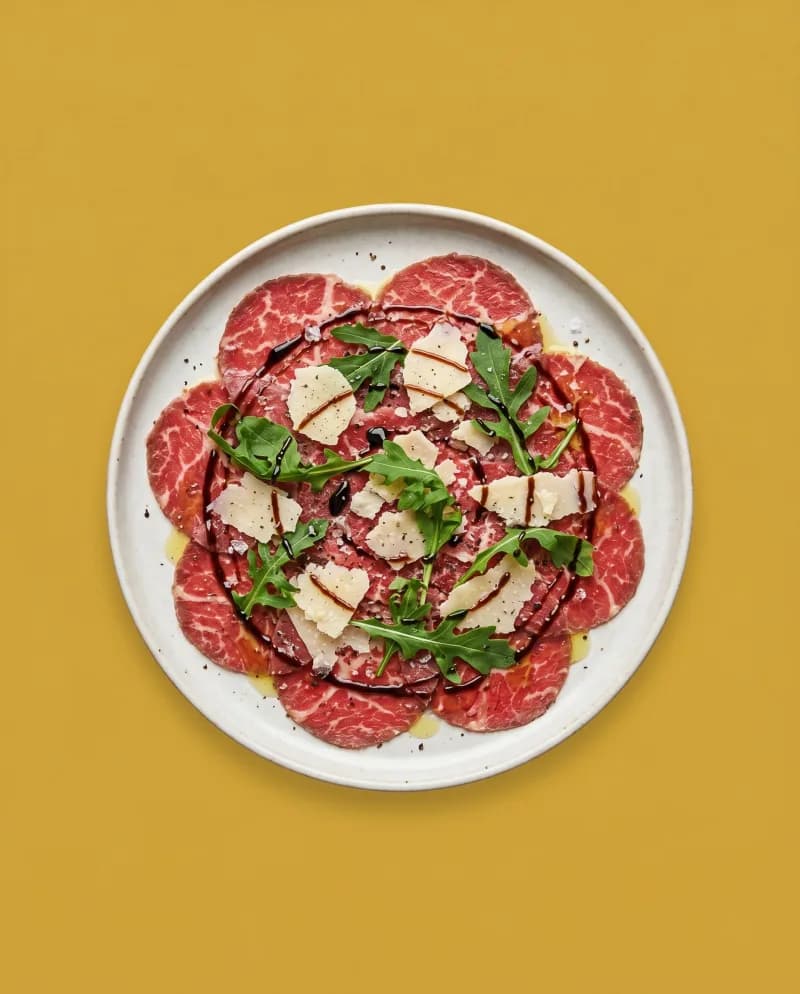 Rundercarpaccio met rucola, Parmezaanse kaas en balsamico op een okergele achtergrond