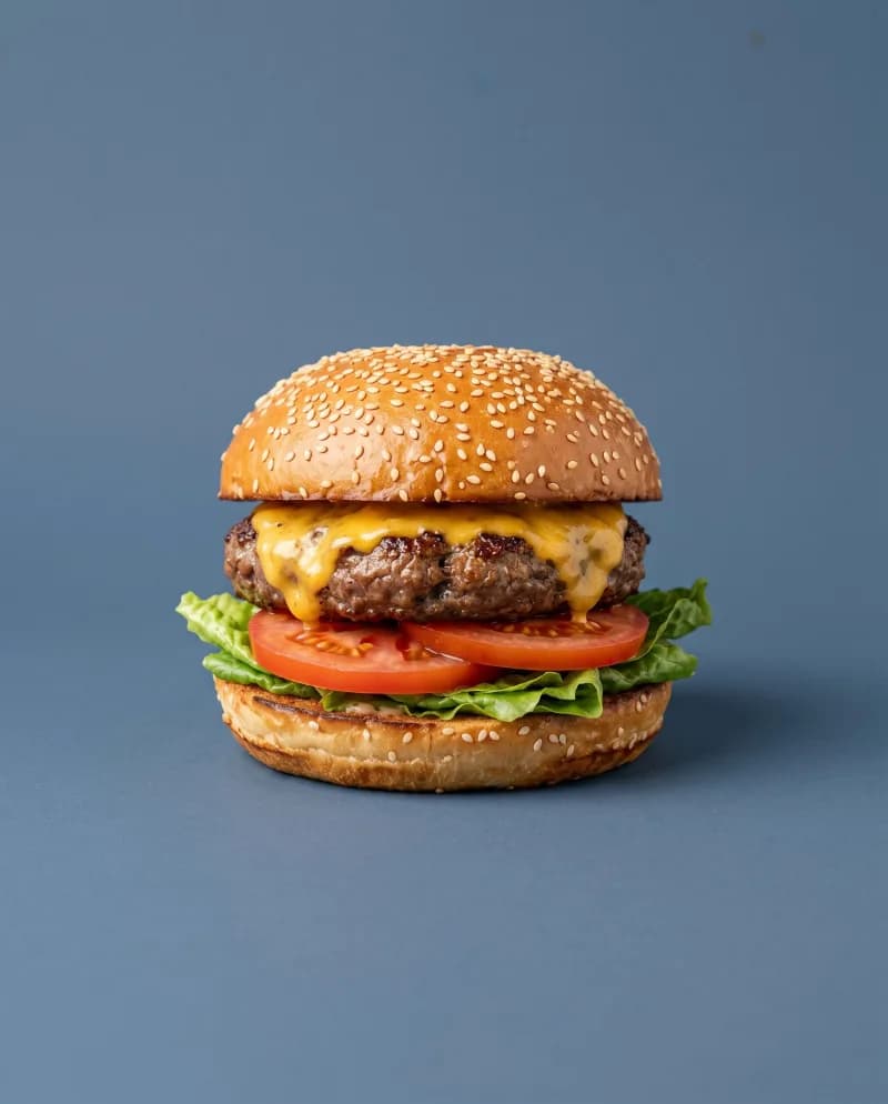 Cheeseburger met smeltende kaas, sla en tomaat op een blauwe achtergrond