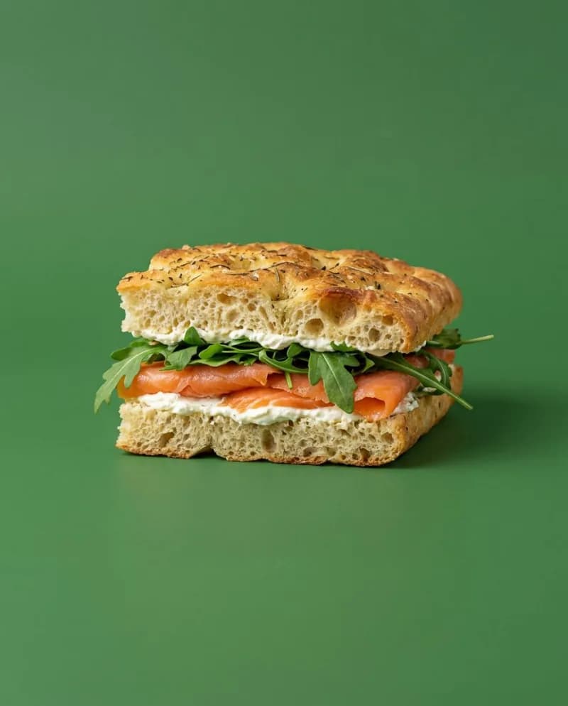 Focaccia-broodje met gerookte zalm, roomkaas en rucola op een groene achtergrond